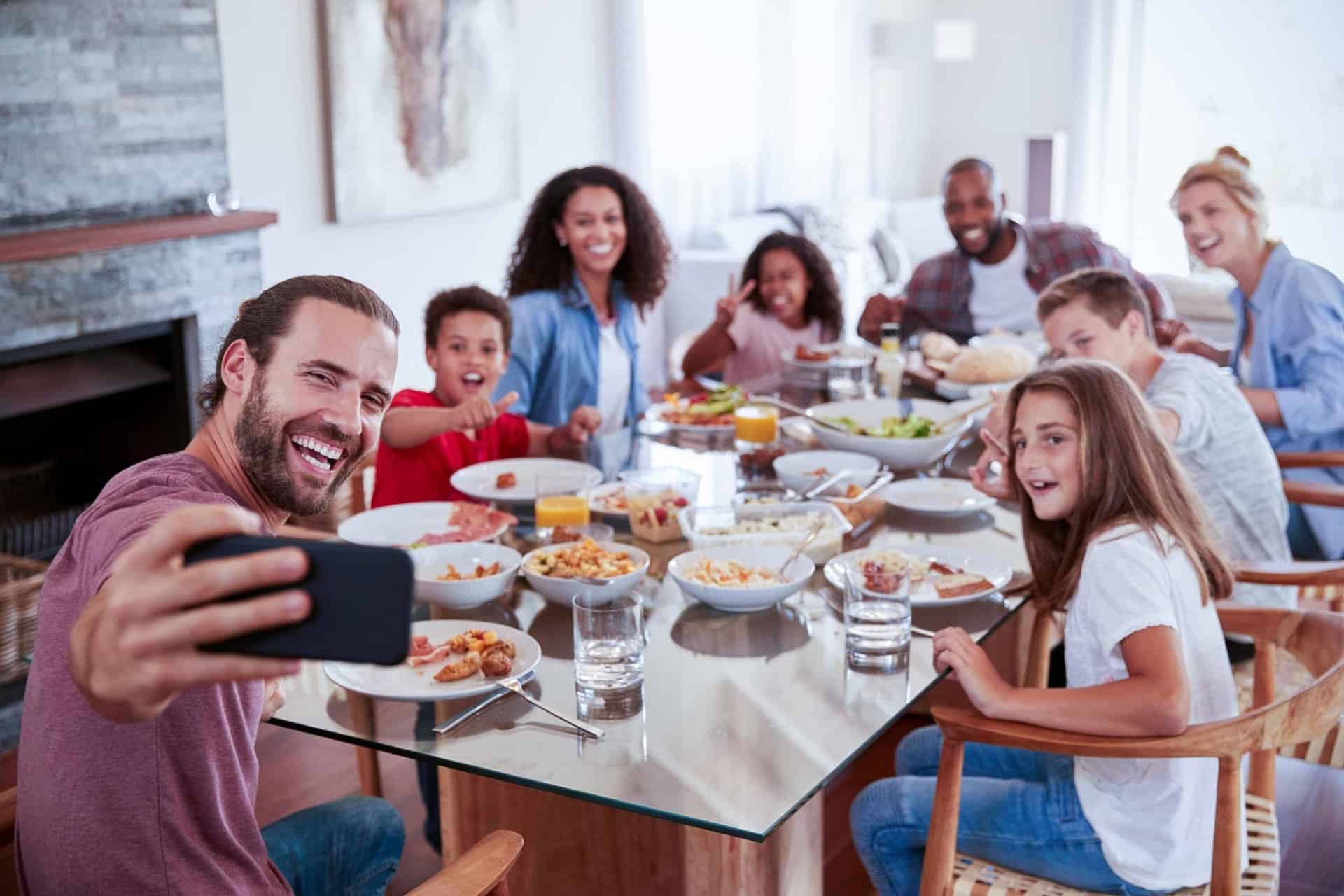 Group of 2 families posing for a selfie around a set dining room table