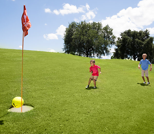 Kids playing Footgolf by kicking a soccer ball into a giant golf hole.